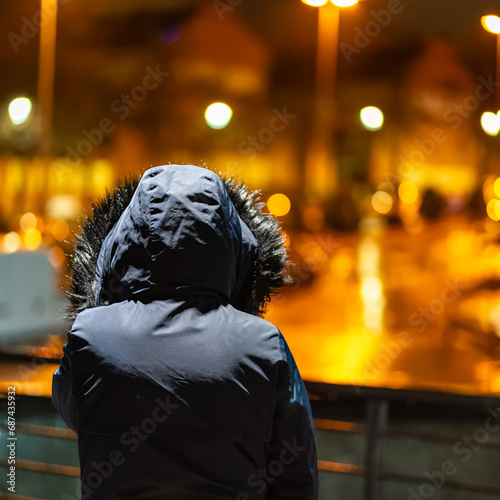 Woman in winter coat while looking at city lights on a rainy day at night.