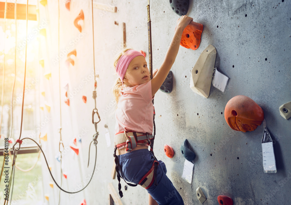 Fototapeta premium A strong baby climber climbs an artificial wall with colorful grips and ropes.