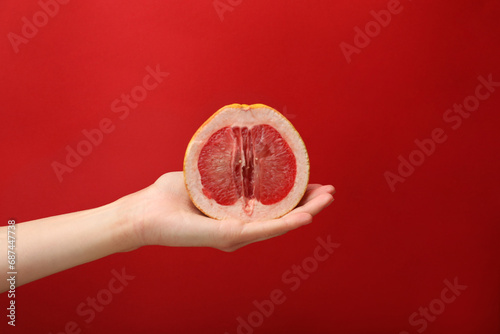 Woman holding half of grapefruit on red background, closeup. Sex concept