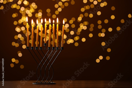 Hanukkah celebration. Menorah with burning candles on table against brown background with blurred lights, space for text