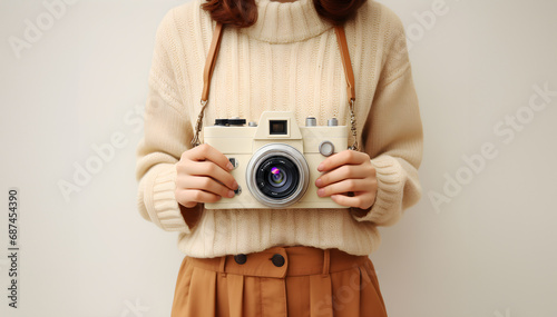 Cropped image of young woman standing and holding an old vintage camera. Female photographer, plain colored background, used as an illustration