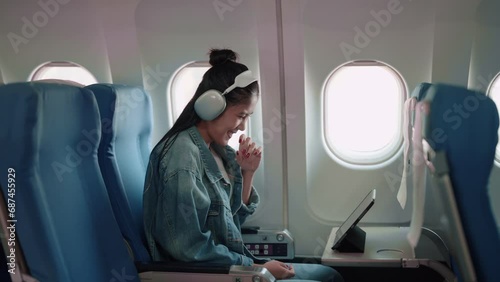 Asian female traveler enjoying a show on her tablet with headphones during the plane journey, anticipating holiday adventures. photo