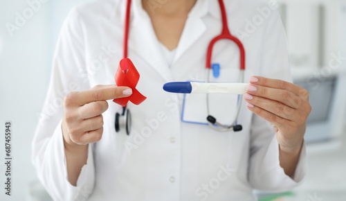Doctor in white coat hold lgbt symbol and in another pregnancy test. Red lesbian society sign and pregnancy detection device close up.