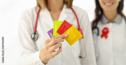 Doctor in white suit hold in hand four condom of different colors. Nurse with red lisbian symbol on her chest. photo