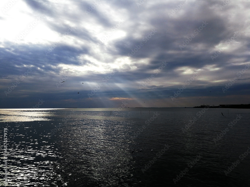 A view of the sea with light from the sun shining through the clouds and hitting the sea surface.
