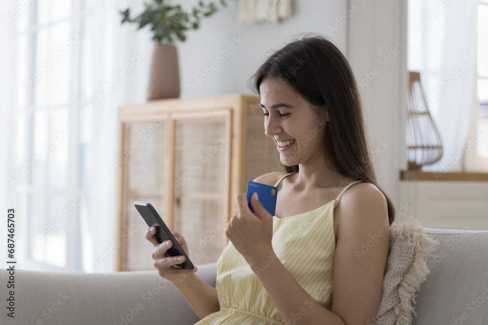 Young pretty woman enjoy e-shopping use debit card and smart phone, buy goods and e-services on-line through web store app, spend money on internet. Electronic commerce, secure e-pay, funds transfer Young pretty woman enjoy e-shopping use debit card and smart phone, buy goods and e-services on-line through web store app, spend money on internet. Electronic commerce, secure e-pay, funds transfer