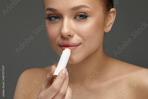  Lips Protection. Beautiful Woman With Happy Face, Sexy Full Lips Applying Lip Balm from Stick. Portrait Of Female Model With Natural Makeup.