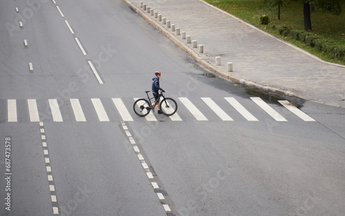 Man crosses the road at a pedestrian crossing and carries a bicycle next to him. View from above.