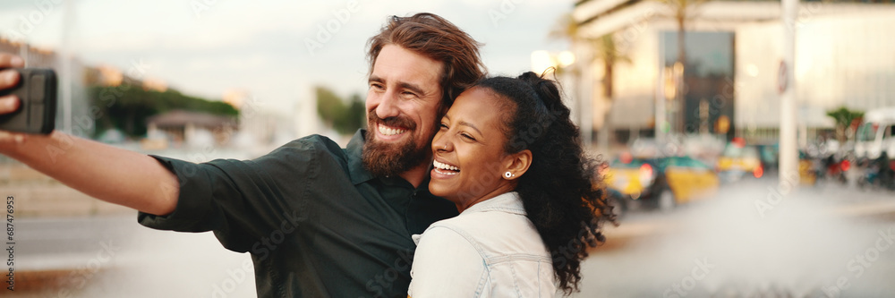 Closeup of smiling interracial couple taking a selfie on fountain background. Close-up, man and woman video chatting using a mobile phone - obrazy, fototapety, plakaty 