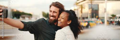 Closeup of smiling interracial couple taking a selfie on fountain background. Close-up, man and woman video chatting using a mobile phone photo