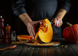 The cook cuts a pumpkin with a kitchen knife on a wooden cutting board. The process of preparing ingredients for a seasonal autumn dish in a restaurant kitchen.