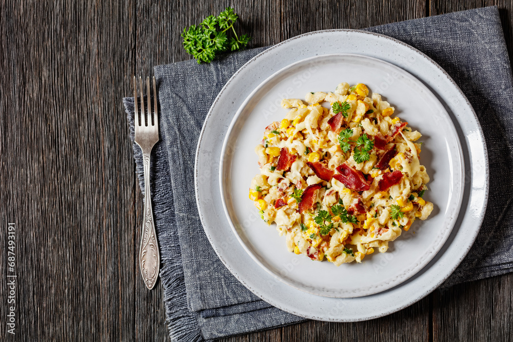 macaroni and cheese with corn, bacon topped with panko breadcrumbs on plate on dark wooden table with fork, horizontal view from above, flat lay, free space macaroni and cheese with corn, bacon topped with panko breadcrumbs on plate on dark wooden table with fork, horizontal view from above, flat lay, free space
