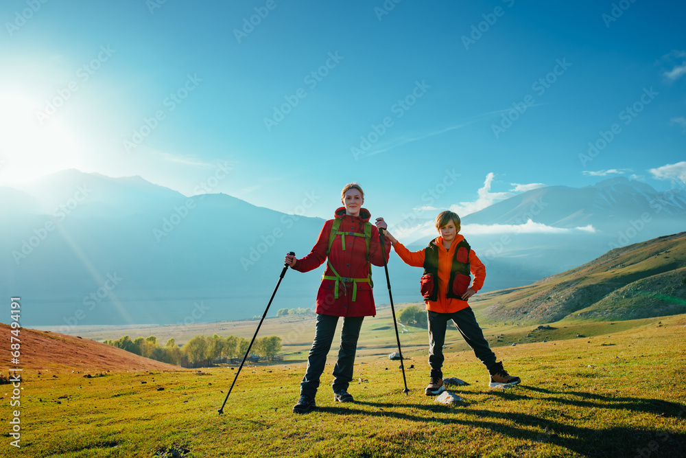 Young woman tourist with son standing in green mountain valley at sunny day