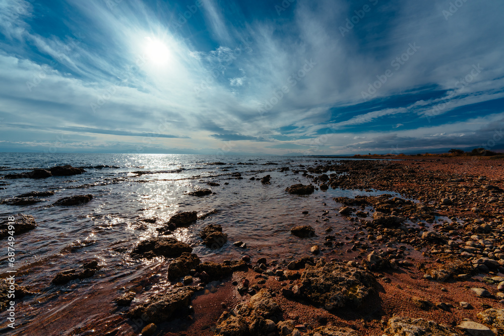Fototapeta premium Rocky shore of lake in sunlight, wide angle view