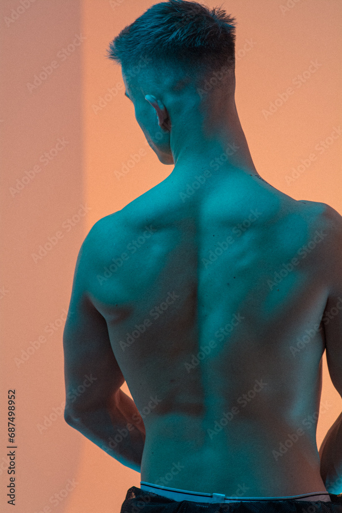 A handsome, inflated guy stands with his back, with a naked torso