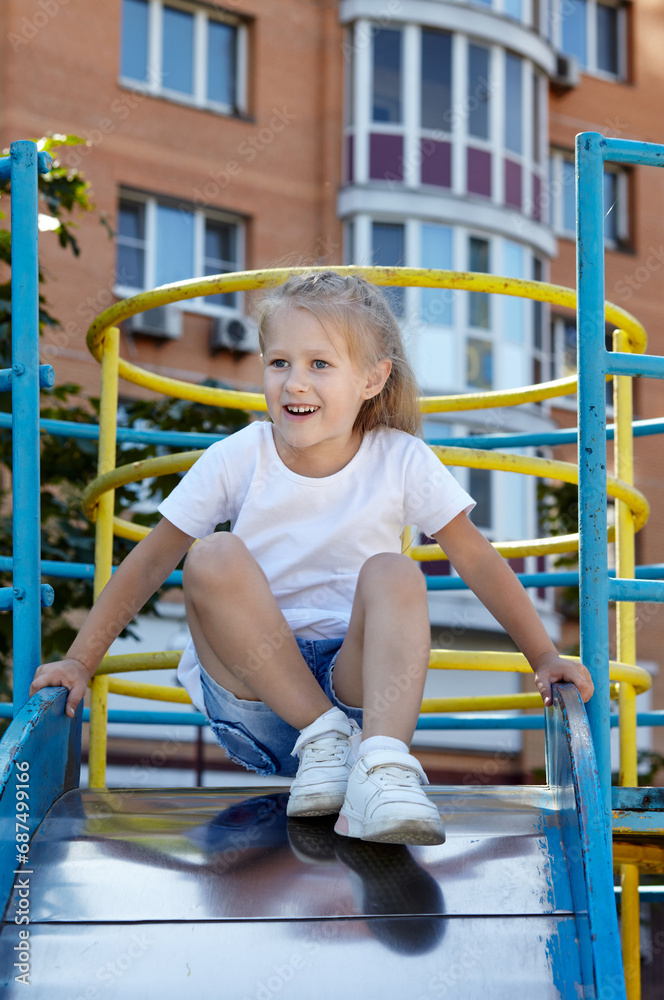 Little girl playing on a slide in a playground in the summer city park. Childhood, leisure and people concept - happy child rest and have a good time Little girl playing on a slide in a playground in the summer city park. Childhood, leisure and people concept - happy child rest and have a good time
