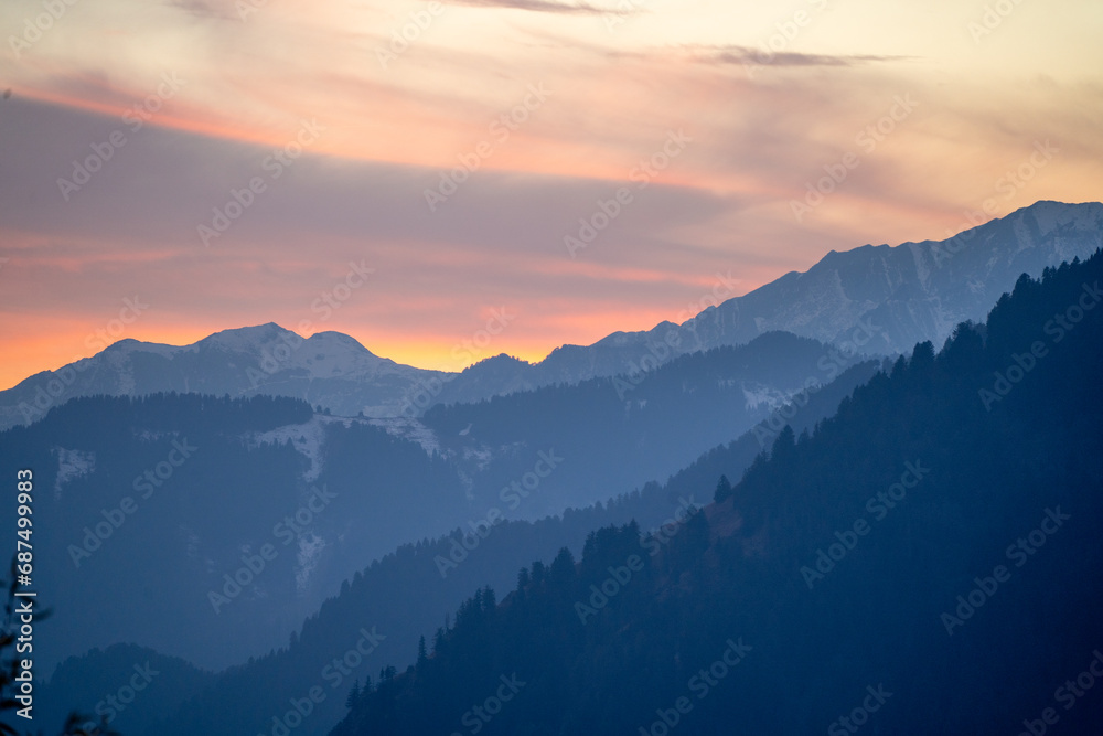 red orange dusk dawn colors over snow covered himalaya mountains and fluffy clouds showing hill stations in jhibbi kullu manali