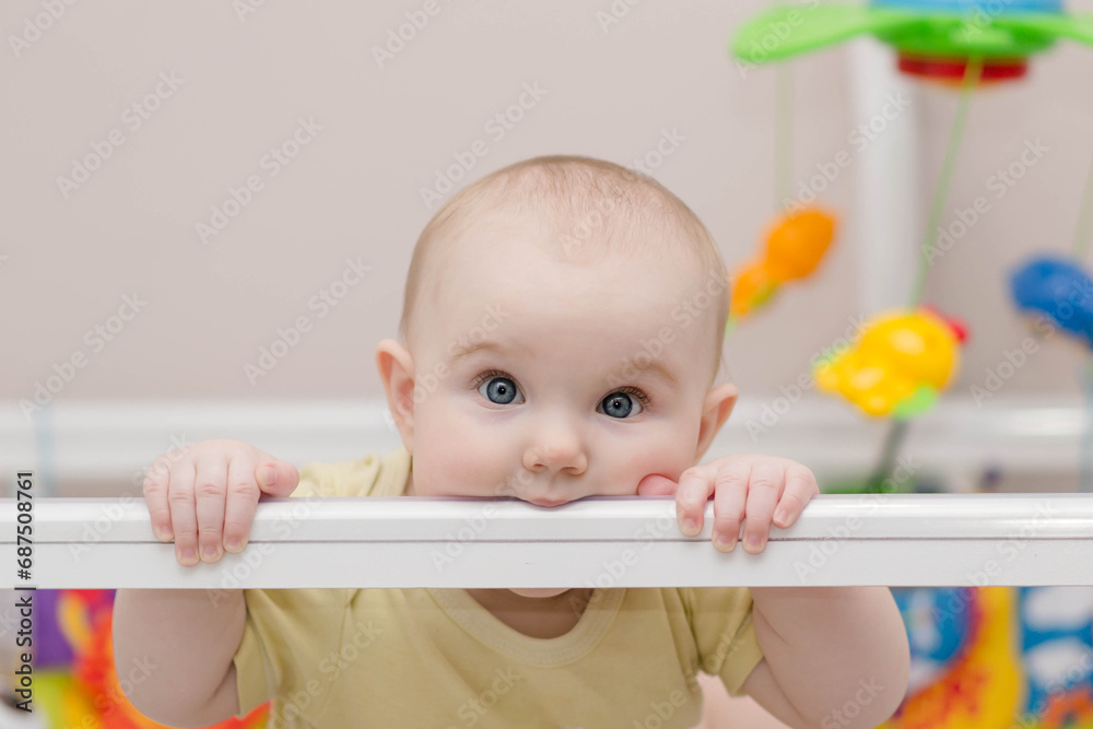 concept of teething, childhood and people - cute little baby lying holding on to her crib and gnawing on it concept of teething, childhood and people - cute little baby lying holding on to her crib and gnawing on it