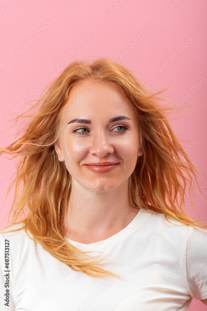 Fototapeta premium Portrait of young round-faced woman with blond hair. Girl on pink background looks to the side.