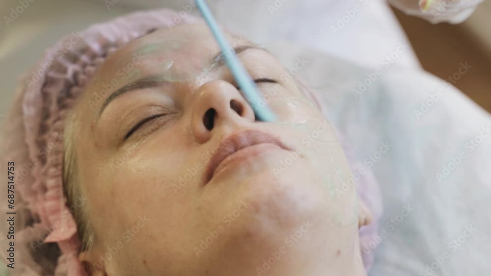 A cosmetologist spreads a cosmetic gel mask onto a womans face with a spatula. Professional procedure in a spa salon. A cosmetologist spreads a cosmetic gel mask onto a womans face with a spatula. Professional procedure in a spa salon.