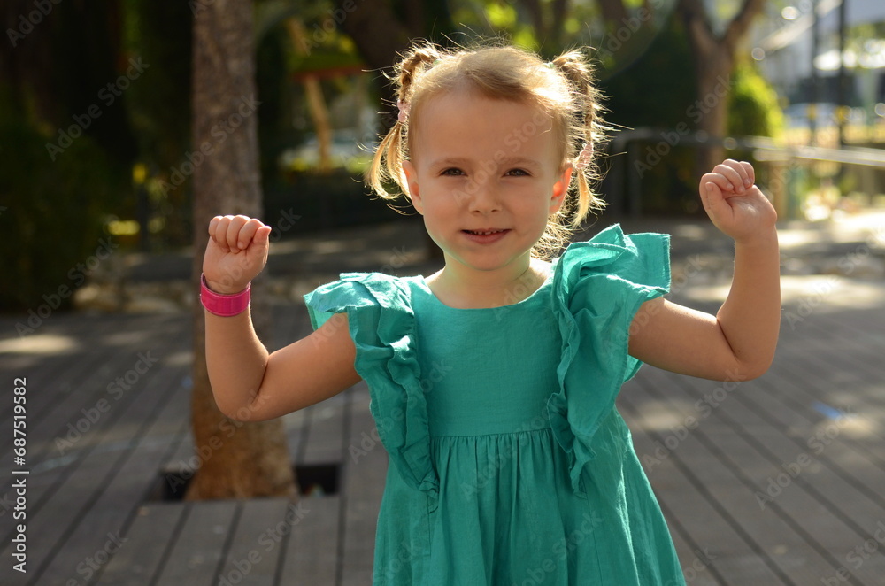 A funny girl with a sly look. Preschool girl portrait of a cheerful girl in a green dress with two pigtails.
