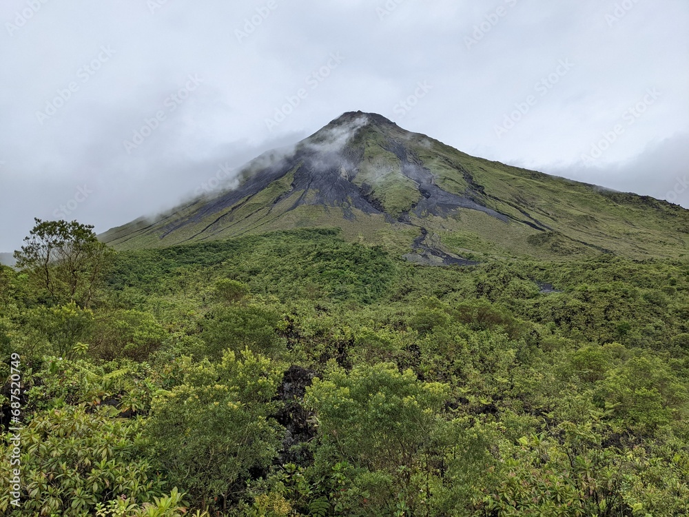 Arenal Volcano with cloud surrounding the summit in La Fortuna, Costa Rica. Green foliage and tropical jungle. Arenal Volcano with cloud surrounding the summit in La Fortuna, Costa Rica. Green foliage and tropical jungle.