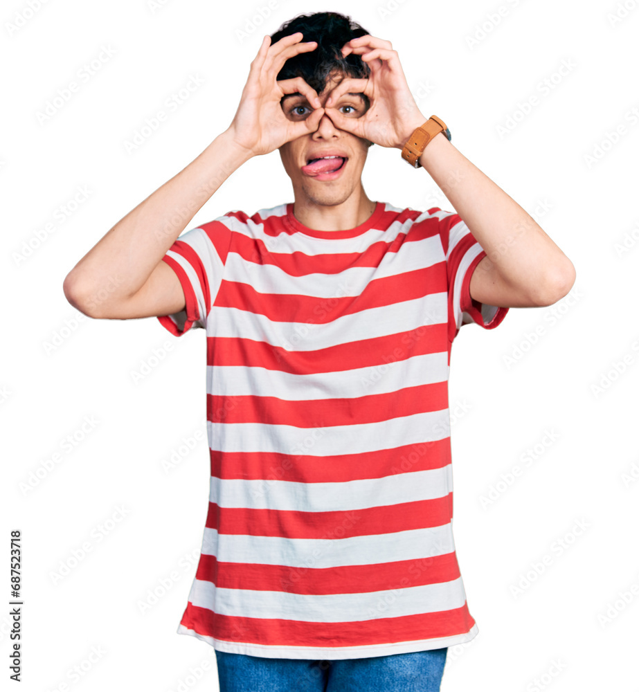 Handsome hipster young man wearing casual striped t shirt doing ok gesture like binoculars sticking tongue out, eyes looking through fingers. crazy expression. Handsome hipster young man wearing casual striped t shirt doing ok gesture like binoculars sticking tongue out, eyes looking through fingers. crazy expression.