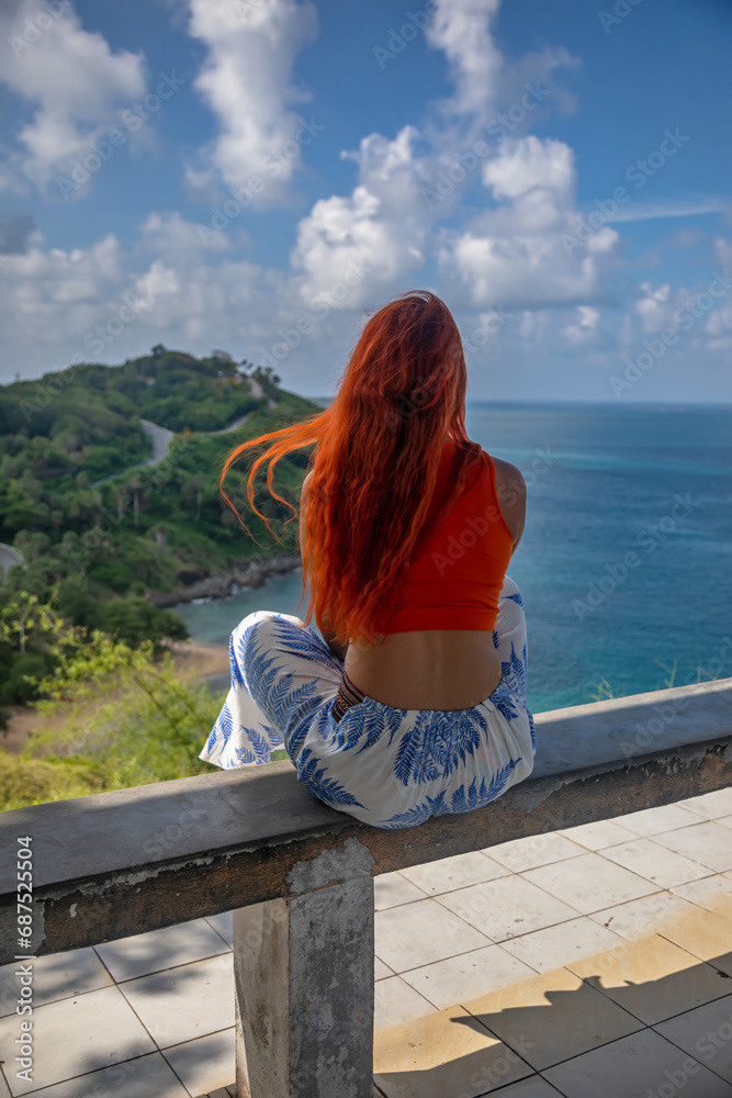 Beautiful red-haired girl on the top of the mountain. Beautiful view of the sea and the island. Sunny summer day.