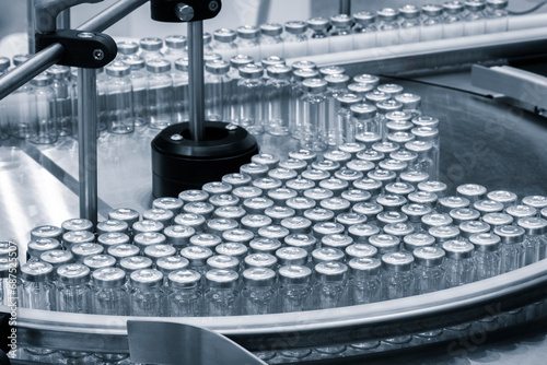 Vaccine production in a pharmaceutical factory, conveyor with the glass jars, modern pharmaceutical factory. Closeup of ampules are being filled with vaccine