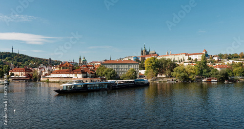 A boat is sailing on a river with a cityscape in the background. Pleasure boat on the Vltava pier in the fall. View of Prague.