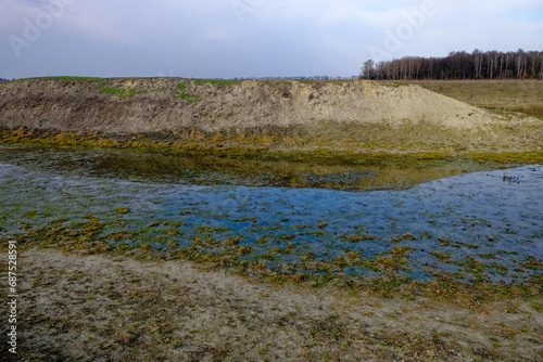 Fototapeta Naklejka Na Ścianę i Meble -  A landscape photo captures a shallow body of water with green algae covering the surface, surrounded by a dirt embankment.