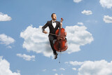 Male musician in a black suit and bow-tie sitting on a cloud playing a cello