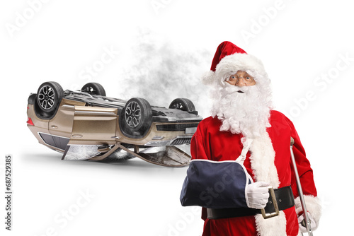 Santa claus with injured arm leaning on a crutch in front of a SUV turned upside down