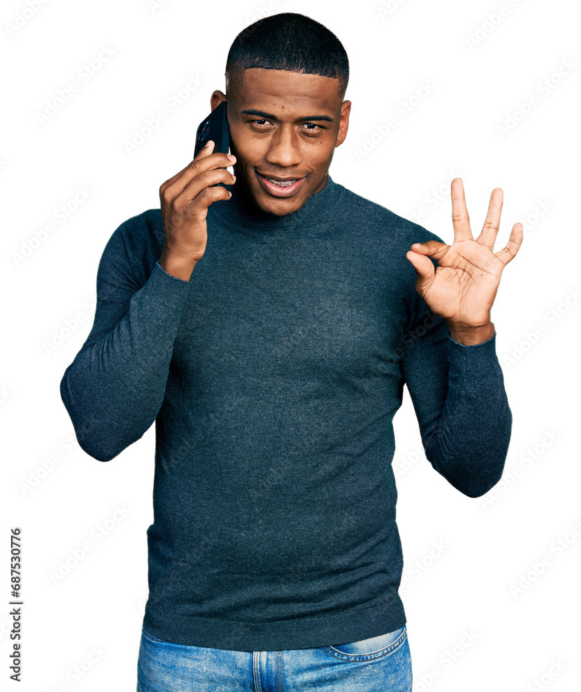 Fototapeta premium Young black man having conversation talking on the smartphone doing ok sign with fingers, smiling friendly gesturing excellent symbol