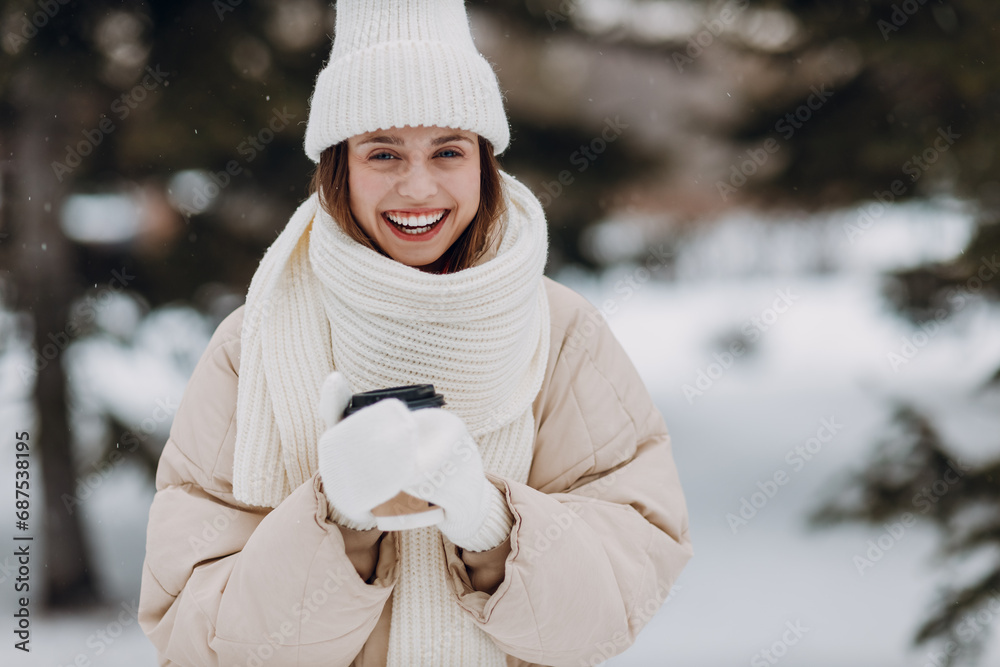 Obraz premium Happy smile young woman with coffee hot drink cup enjoys winter weather at snowy winter park