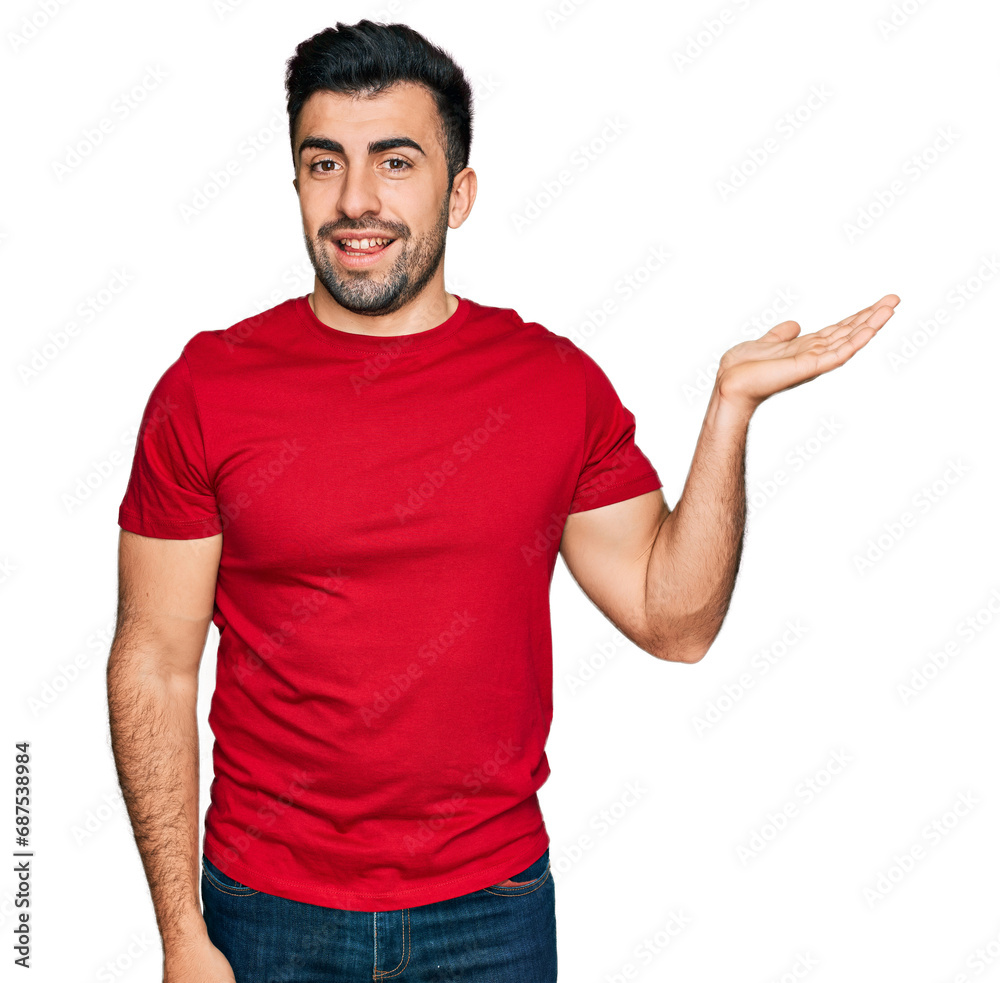 Hispanic man with beard wearing casual red t shirt smiling cheerful presenting and pointing with palm of hand looking at the camera. Hispanic man with beard wearing casual red t shirt smiling cheerful presenting and pointing with palm of hand looking at the camera.