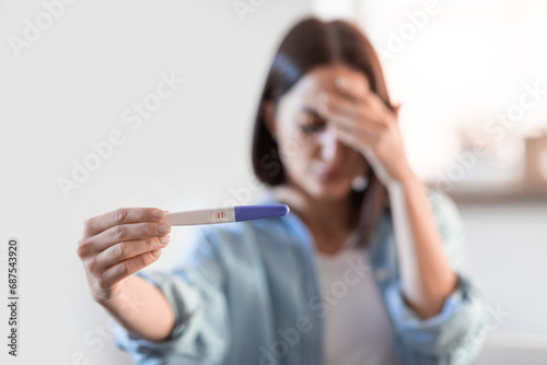 Upset lady holding positive pregnancy test at home, covering face photo