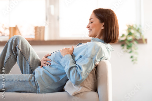 Pregnant Young Woman Hugging Belly Resting On Sofa At Home © Prostock-studio