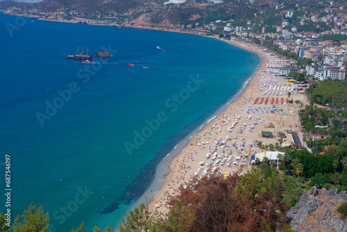 Beautiful top view of blue sea ocean water and beach shore with lots many of people tourists, green trees in summertime and bright sunlight sun.Tourism destination,vacation,holiday