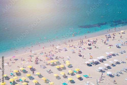 Beautiful top view of blue sea ocean water and beach shore with lots many of people tourists under white yellow umbrellas in summertime and bright sunlight sun.Tourism destination,vacation,holiday