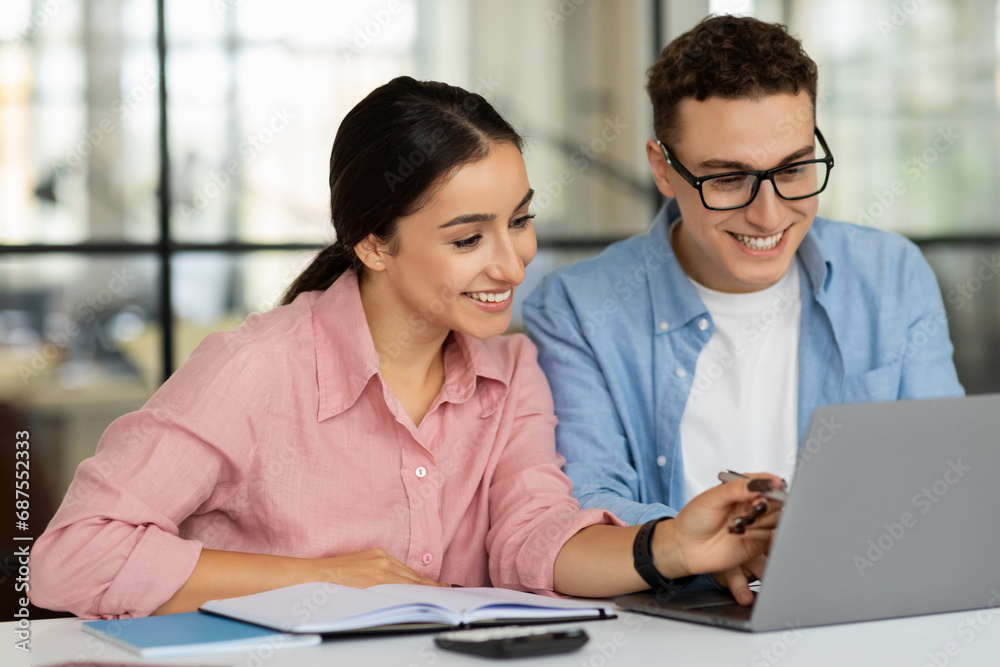 Obraz premium Smiling millennial arab lady and european guy manager planning startup app on laptop