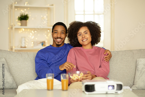 Millennial black spouses watching film cuddling on couch at home
