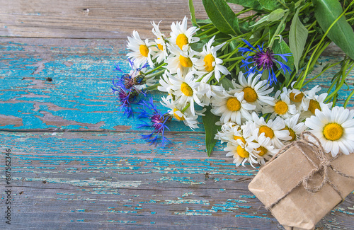 Bouquet of white daisies and bluecorns and handmade gift box on the old blue paint wooden background; space for text