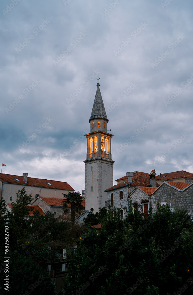 Illuminated bell tower of an ancient church against a dark sky in the evening
