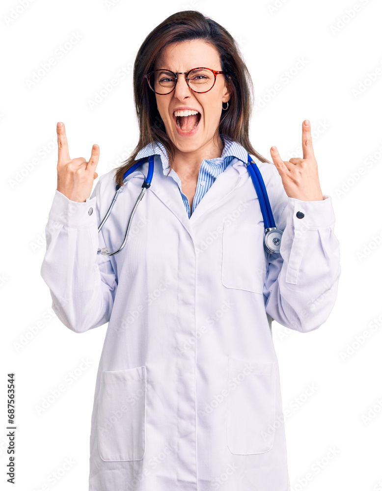 Young beautiful woman wearing doctor stethoscope and glasses shouting with crazy expression doing rock symbol with hands up. music star. heavy concept. Young beautiful woman wearing doctor stethoscope and glasses shouting with crazy expression doing rock symbol with hands up. music star. heavy concept.