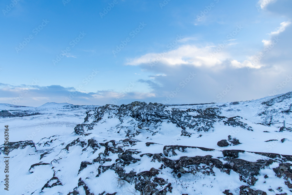 Close up of snow covered lava rock formations near Kerid volcanic crater lake on south Iceland, along the Golden Circle against a blue clearing sky with snow clouds