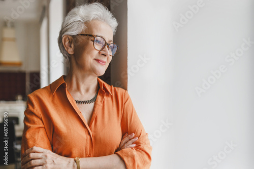 Canvas Print Side view of pretty charming grandmother in orange shirt and glasses leaning aga