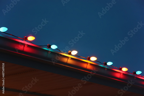A cheerful and colorful holiday background with a closeup of a house roof decorated with detailed and glowing Christmas lights at dusk.