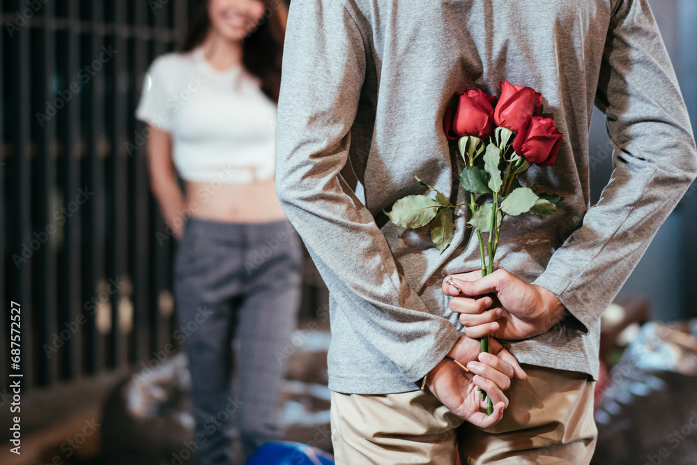 Fototapeta premium Asian man hiding roses to surprise his girlfriend on dating in Valentine's, Anniversary or birthday, focus on flower, attractive couple having romantic on rooftop