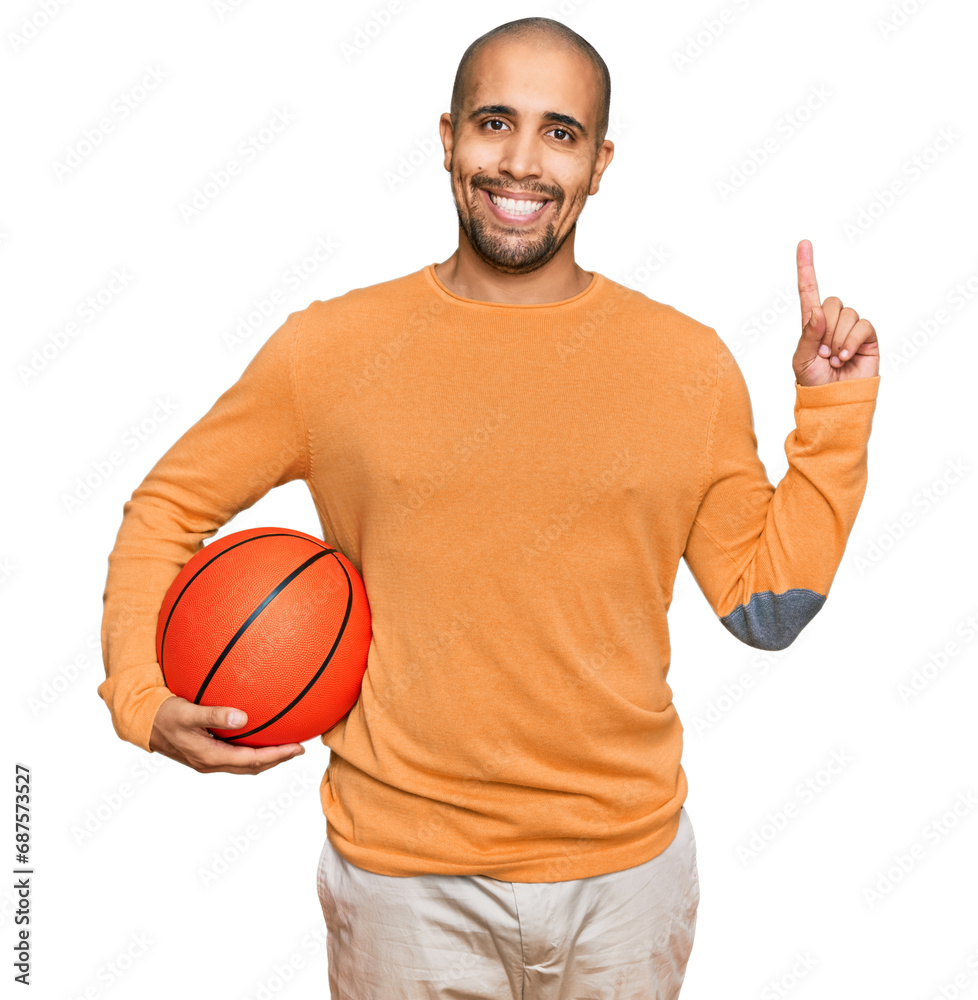 Hispanic adult man holding basketball ball surprised with an idea or question pointing finger with happy face, number one Hispanic adult man holding basketball ball surprised with an idea or question pointing finger with happy face, number one